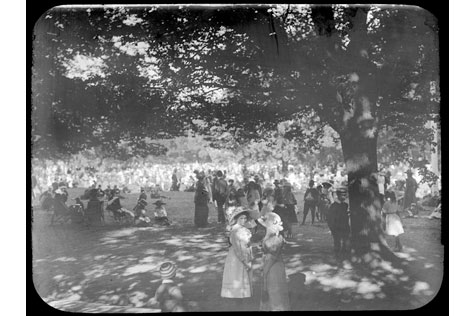 Large group of people dress in clothes from the 1900s outdoors, standing under trees