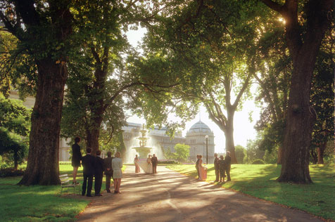 Wedding party under trees, fountain and Exhibition Building behind.