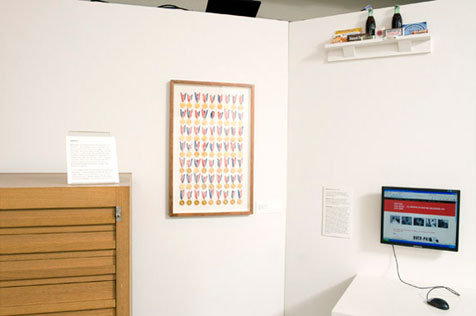 South-west corner of gallery, with wooden display cabinet on left, computer screen on right with shelf above, and frame of medals on ribbons at centre