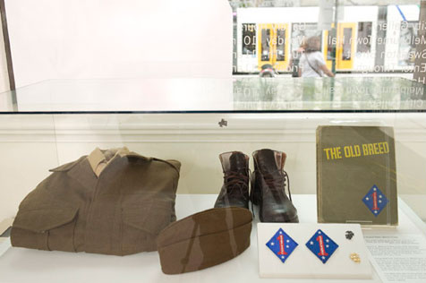 Glass tabletop display case housing marine uniform and boots, with a book titled The Old Breed on the right