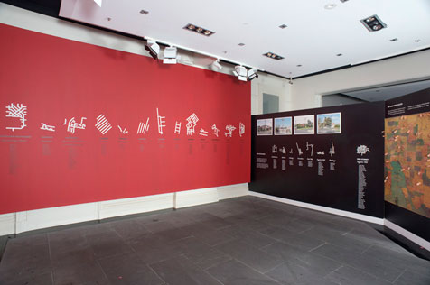 Exhibition installation of white maps on red and black walls