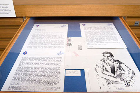 Open drawer in a wooden display case, holding three typed pages, an envelope and, on the right, an ink sketch of a young man