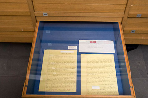 Open lower drawer in a wooden display case, holding two handwritten yellow pages and an envelope with a red ‘air mail’ stamp on it
