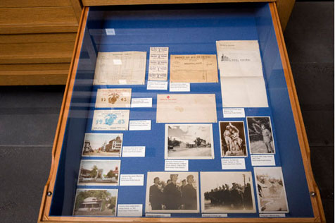 Open drawer in a wooden display case, holding nine black-and-white photos, cards and several letters