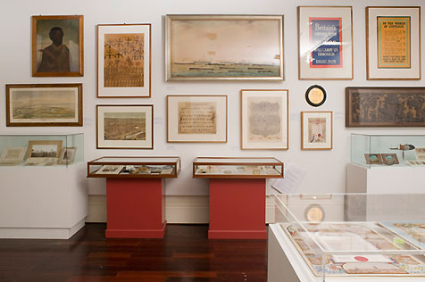 Gallery interior showing five display cases and 12 artworks on the wall behind