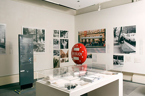 Gallery’s north-east corner, with 14 photographs on the walls, glass display case in foreground and red ‘life buoy’ in the midfield