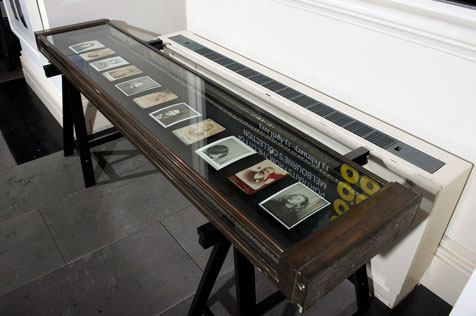 Glass and dark wood display table with eleven black and white and sepia photos