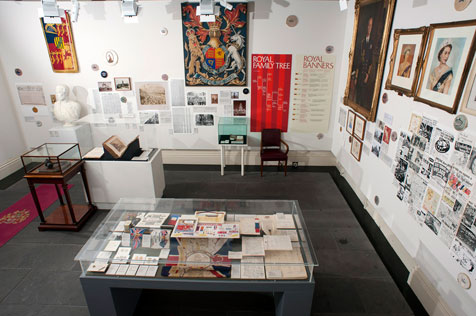 Overview of the gallery whowing glass display case, brightly coloured tapestries, white bust, royal banners and other ephemera