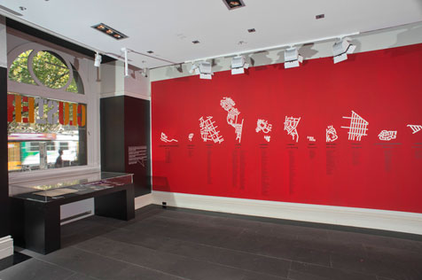 Exhibition installation of black and glass case and stylised white maps on red wall