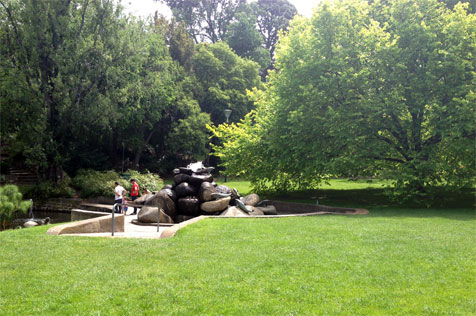 Lawn, trees and sculpture by pond.
