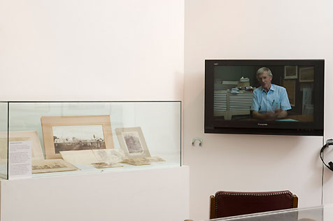 Television screen display and glass-topped case at left containing several sepia photographs