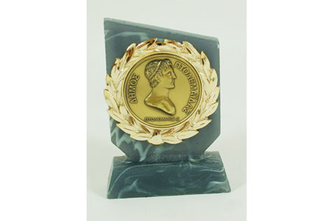 Gold coloured medal featuring silhouette of of Alexander the Great and olve wreath mounted on a grey-blue plastic stand