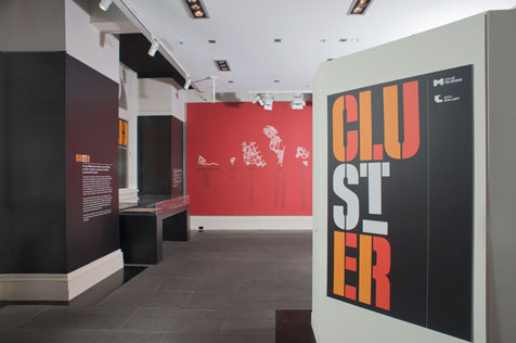 Entrance to exhibition with larger black, orange and white 'Cluster' poster