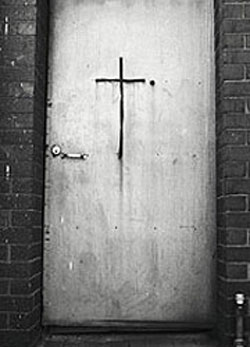 black and white photograph of a simple cross on a wooden door