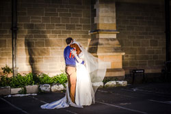 A man and a woman in a wedding dress embrace while a light is on them.