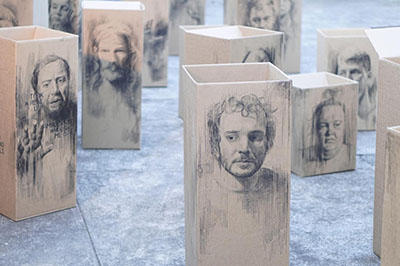 Wooden boxes wth portraits of people drawn on them in black