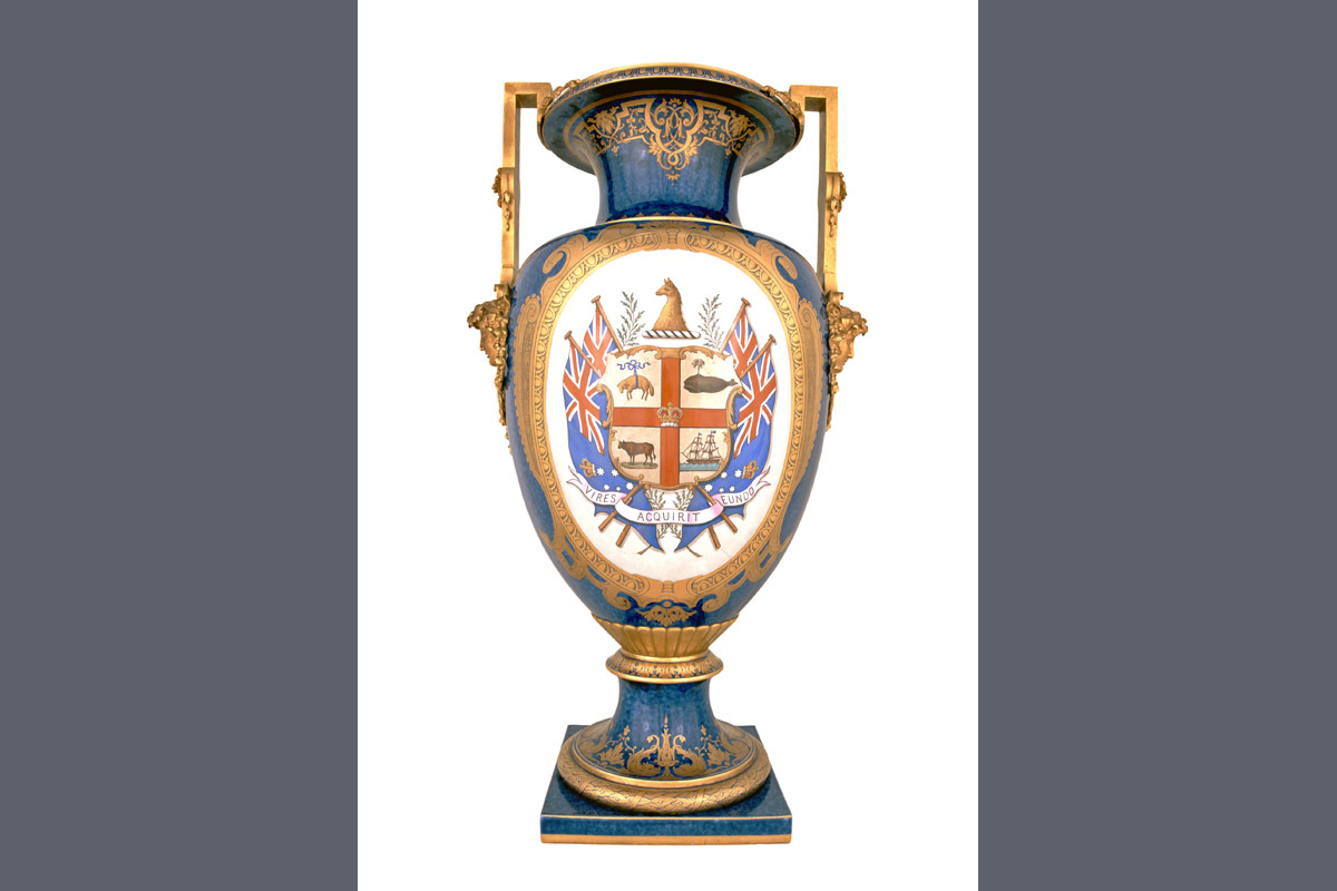 Blue urn with bronze handles, golden embellishments and white oval panel with City of Melbourne coat of arms and Colony of Victoria flags