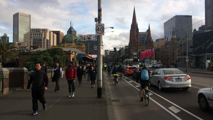 Princes Bridge showing the wide bike lane which is between the busy raised footpath and the moving traffic, separated by wide line markings.
