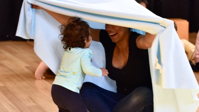 An adult playing with a child holding a blanket over themselves