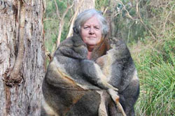 A woman wearing a large possum skin cloak looks at the camera.