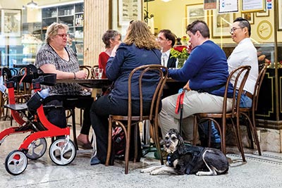 A group of people seated at cafe, with a mobility scooter and assistance dog
