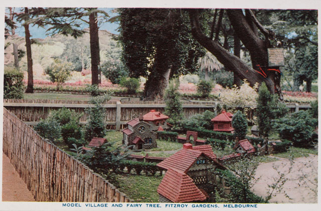 The Tudor Village showing miniature red-roofed buildings among small trees and shrubs, enclosed by a short wooden fence, large trees in the background Caption reads: 'Model village and fairy tree, Fitzroy Gardens, Melbourne'.