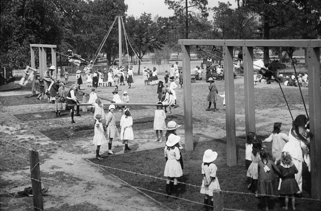 Black and white photo showing young girls playing on swings, see-saws and maypoles.