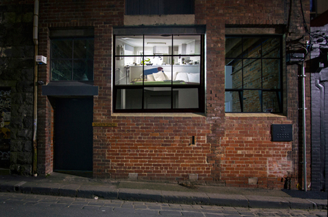 Red brick building facade with image of an interior with furniture projected on its window