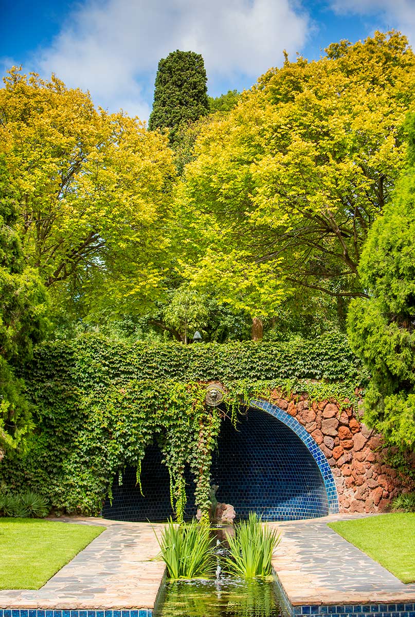 A water feature with a decorative tiled archway covered in green ivy and a long, narrow rectangular pool.