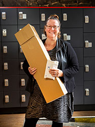 Donna Newman standing in front of post boxes and holding a large cardboard box.