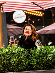 Joanna Gamvros standing behind a planter box and in front of red and white umbrellas at Bar Lourinhã.