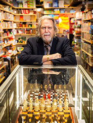 Leighton Hipkins in the Mind Games shop, with chess boards in a display cabinet and shelves filled with games and puzzles.