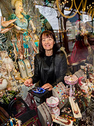 Mel Martino standing behind the shop window displays of jewellery, ornaments and decorations.
