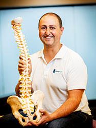 Peter Rentoulis, holding a model of a spine and pelvis bones