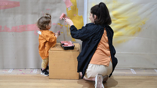 Toddler and adult painting on vertical surface with roller
