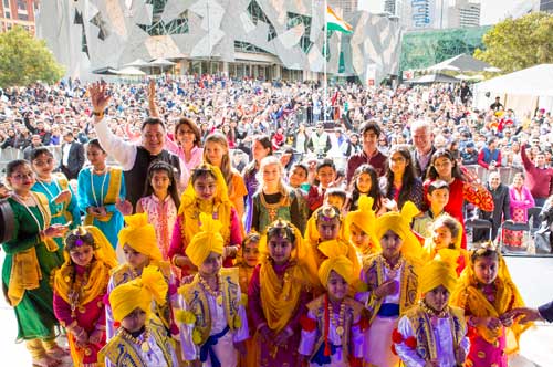 Group of children and adults in Indian traditional dress, posing in a front of a large crowd at Federation Square