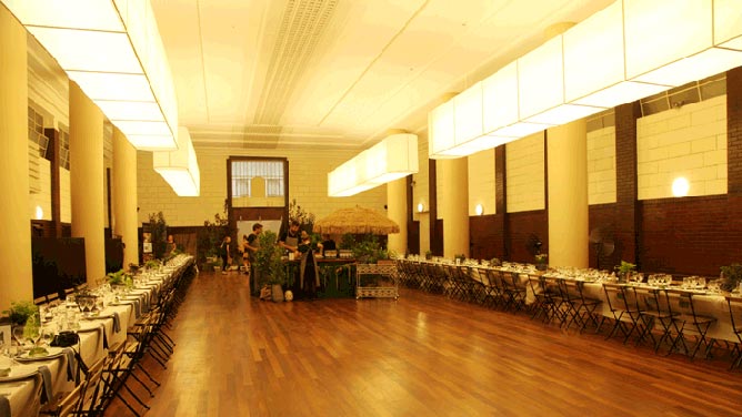 Large hall with wooden floors and feature lights, set up for function with tables and chairs in a long line along opposite edges