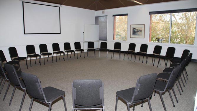 Room with two windows, whiteboard, and approximately 24 chairs arranged in a circle