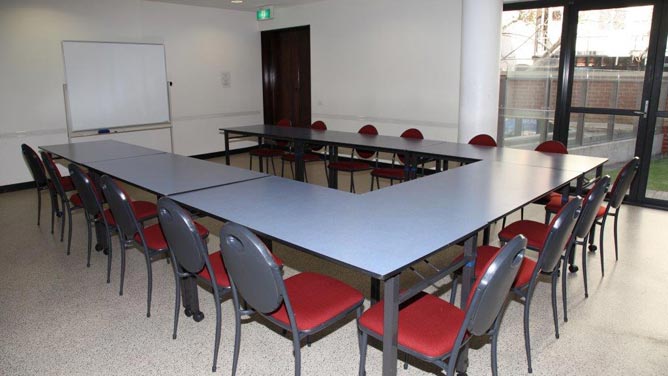 Room with tables and chairs arranged in U-shape, whiteboard, full-height window and external glass door