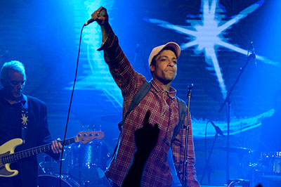 Singer with arm raised holding microphone with bass guitarist in background