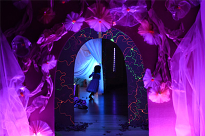 A small child in a dark, ambient lit interior space with a neon lit archway.