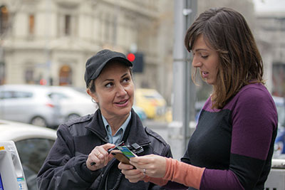 Parking officer helping woman with parking ticket and meter