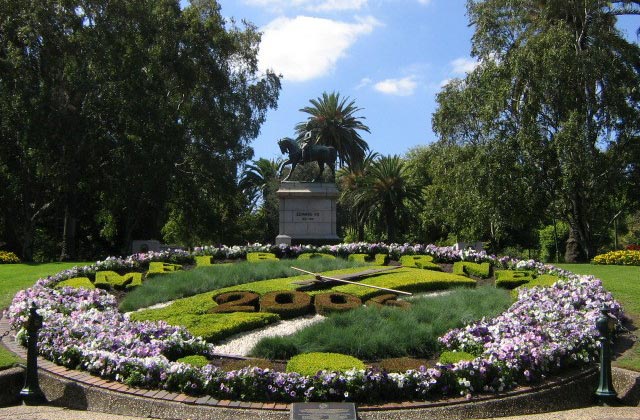 Floral clock planting has '2006' formed by hedges in the centre of the clock, 'Melbourne' formed by hedges along the top edge, and purple flowers along the bottom edge.