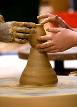 Two pairs of hands touching clay on spinning potters wheel