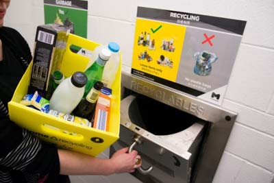 person using a recycling chute, which has an sign above showing what is accepted