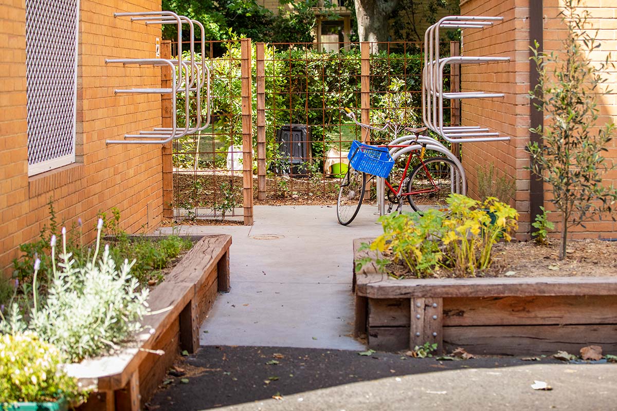 A communal space in the apartment complex with new raised garden beds, vines with climbing frames, and rows of bike hoops.