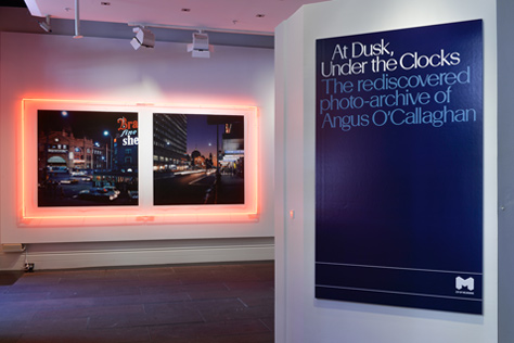 Entrance to the gallery featuring poster and neon-light framed photographs