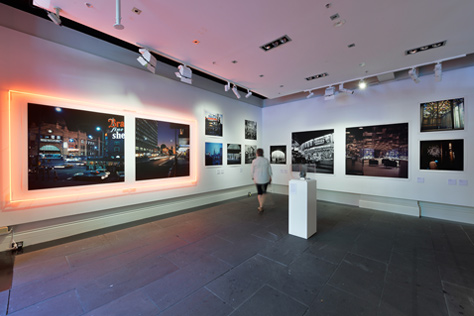 Man standing in the corner of a large white room with photographs covering the walls