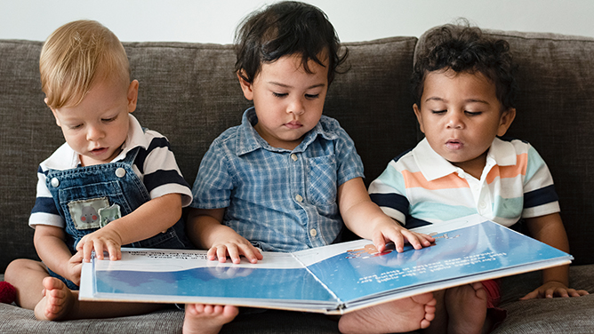three small children sitting on a lounge reading a book