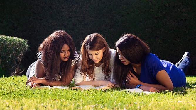 three young women lying on grass studying together
